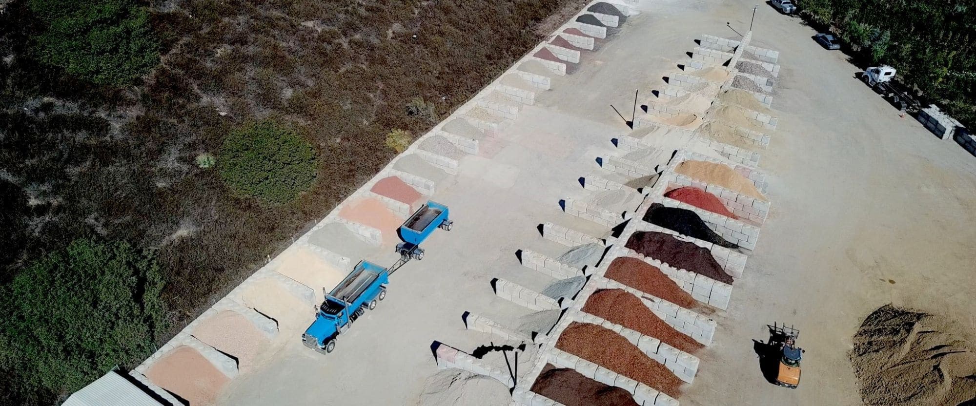 Aerial view of a supply yard with rows of material bins and a dump truck with a trailer